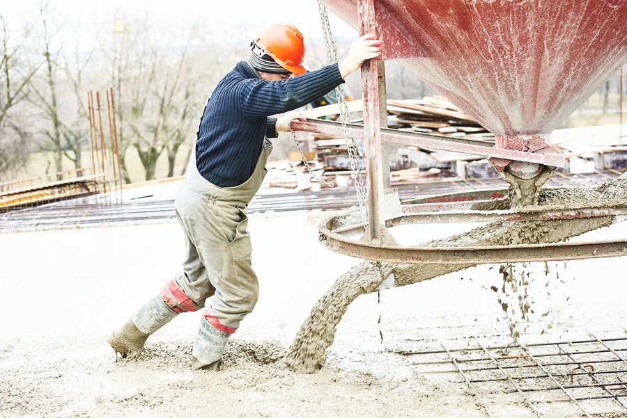 Concreting work. Construction site worker during concrete pouring into formwork at building area with barrel skip in cold weather.